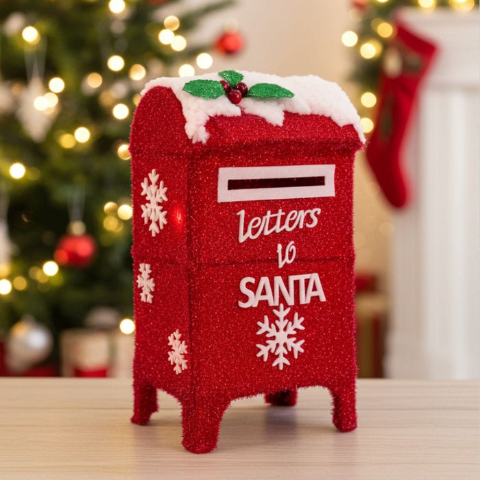 Decorative red mailbox with 'Letters to Santa' text in a festive setting with Christmas tree and stockings.