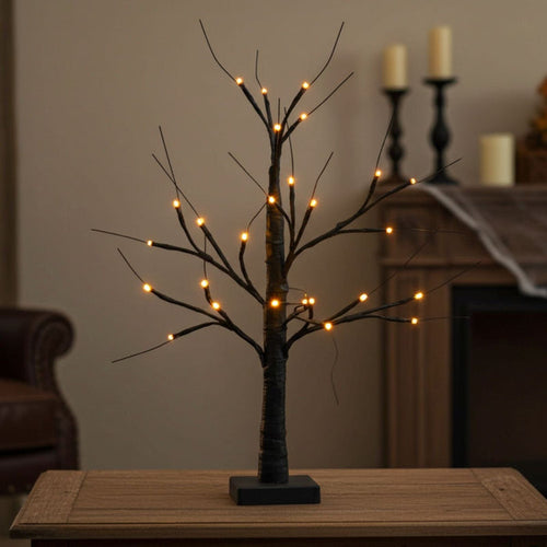 Decorative LED tree on a wooden table with candles in the background