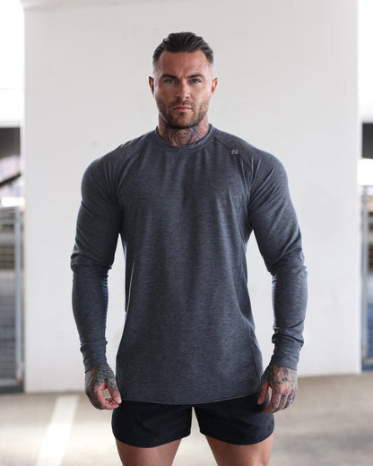 Man wearing a gray long-sleeve athletic shirt and black shorts in an indoor setting.
