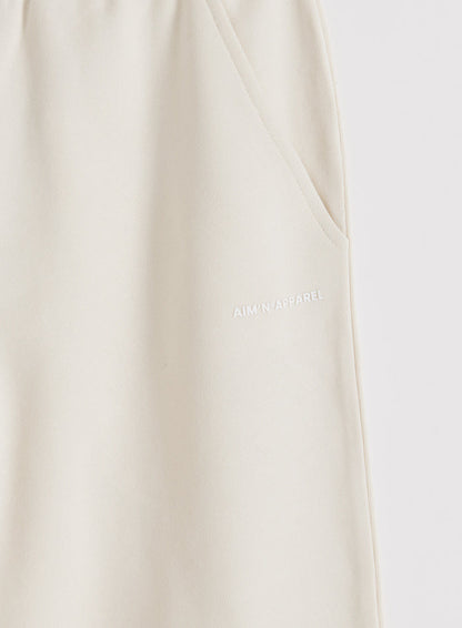 Yksityiskohta Cream Chunky Terry Sweatpants -housuista, joissa on sivutasku ja valkoinen aim'n-logo.