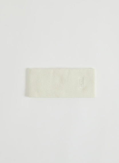 Kermanvärinen neulottu otsapanta logodetaljilla kuvattuna flat lay -asetelmassa