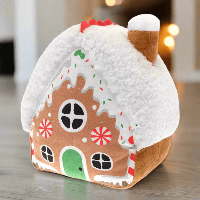 Gingerbread house-shaped door stopper on a wooden floor with a blurred background featuring door and christmas lights