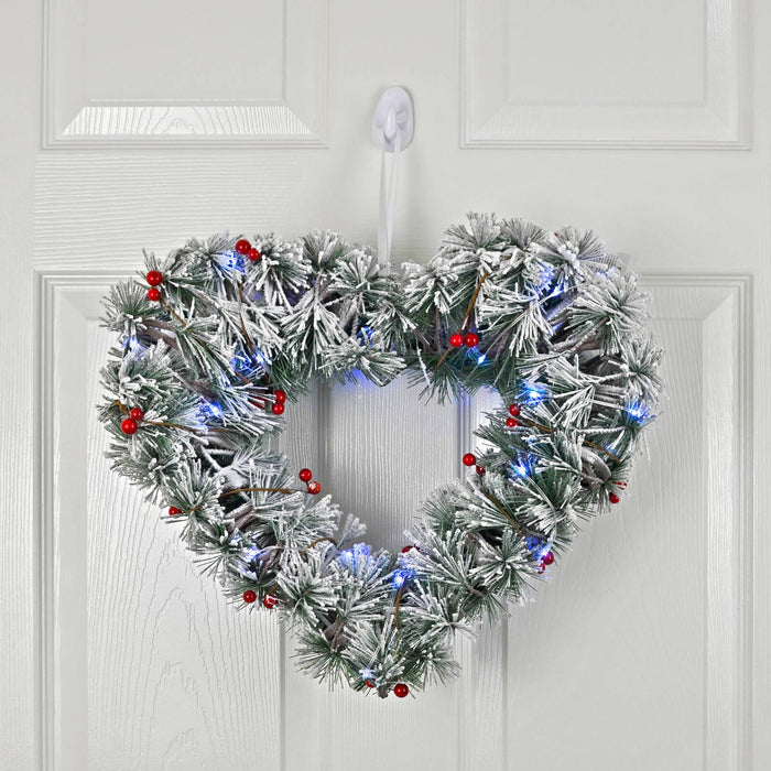 Heart-shaped Christmas wreath with lights and berries on a white door