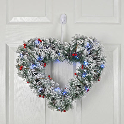 Heart-shaped Christmas wreath with lights and berries on a white door