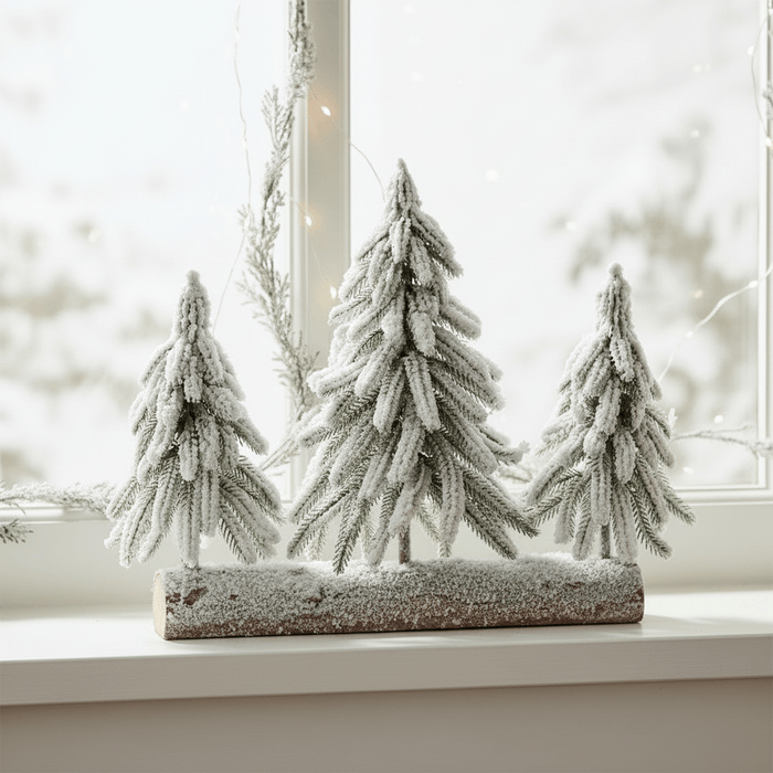 Decorative set of three frosted trees on a log against a blurred window background