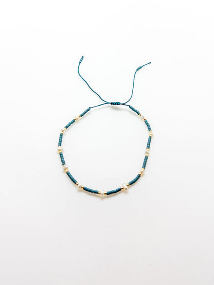 An adjustable teal bracelet with gold accents on a white background