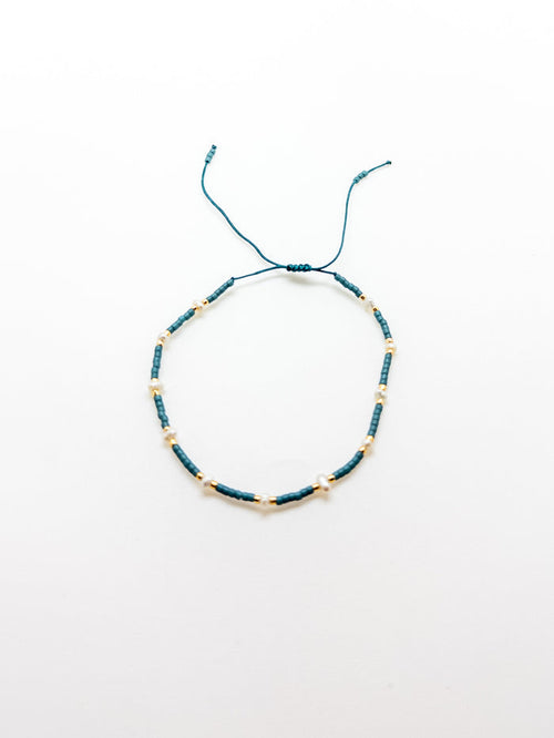 An adjustable teal bracelet with gold accents on a white background